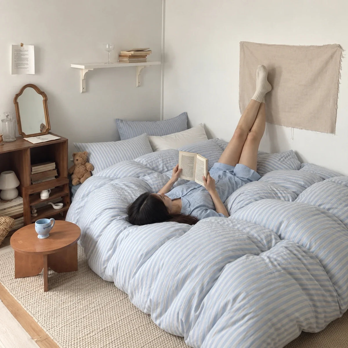 A woman reading on blue striped bedding with her feet resting on the wall.