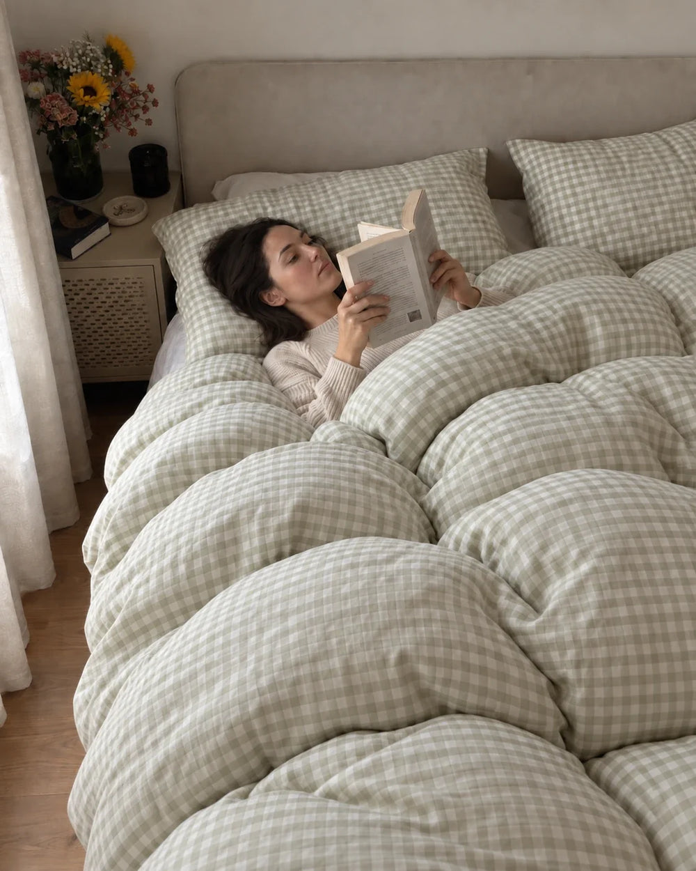 A woman reading under a pale green checked duvet.