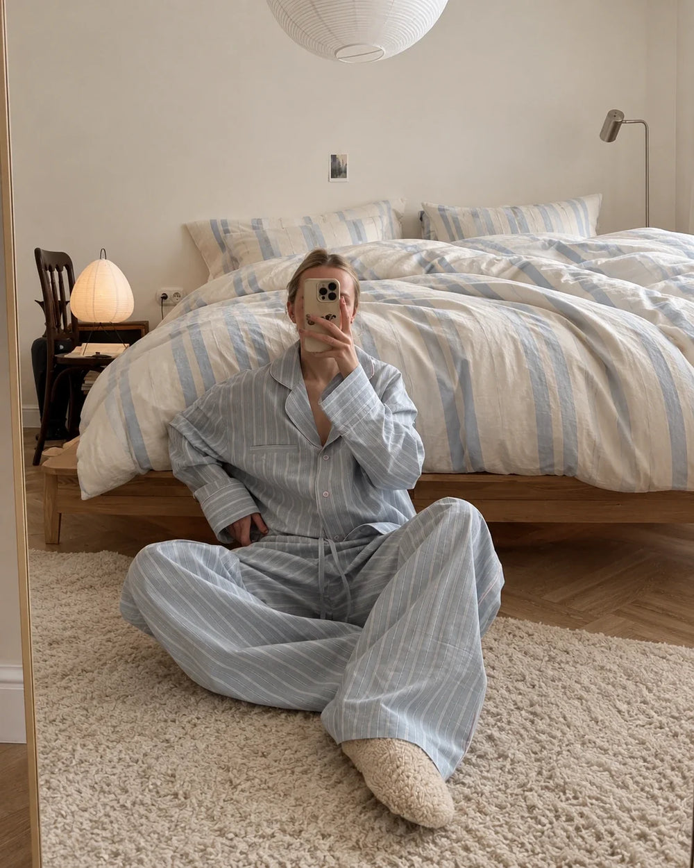 A woman in blue striped pyjamas sitting beside a bed with blue striped bedding.