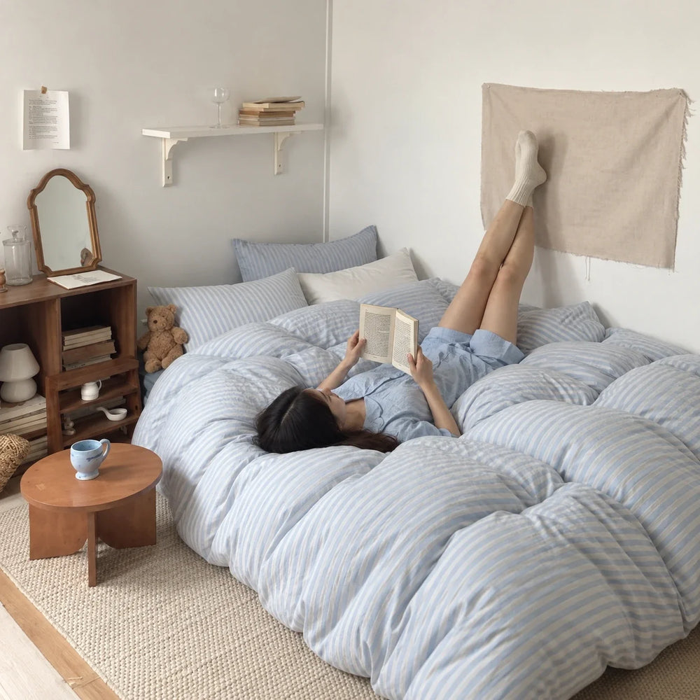 A woman reading on blue striped bedding with her feet resting on the wall.