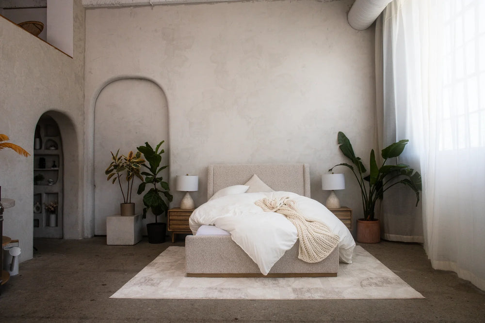 A white duvet piled on a bed in a bright room with plants and arched doorways.