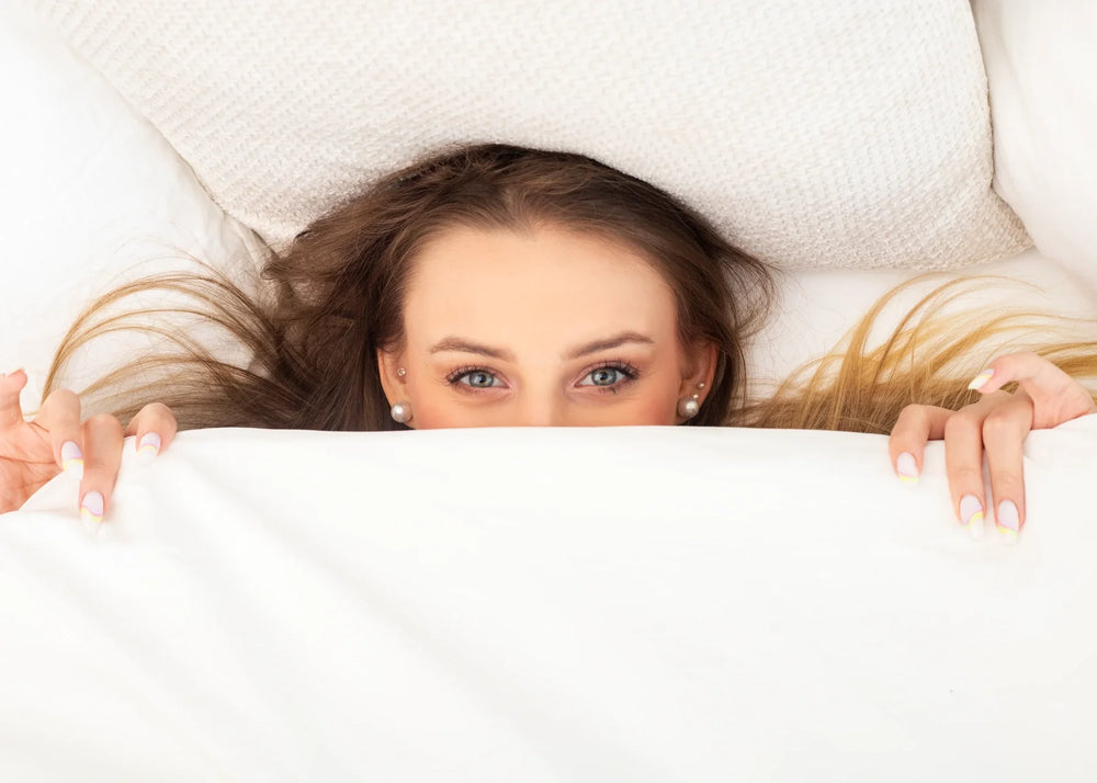 A woman peeking over the edge of a white duvet.