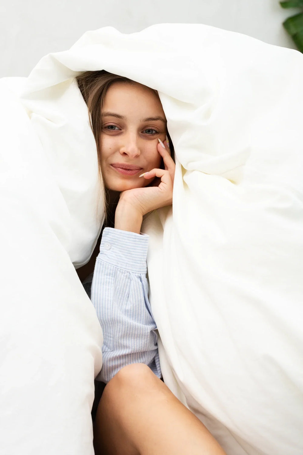 A woman resting under a white duvet pulled over her head.