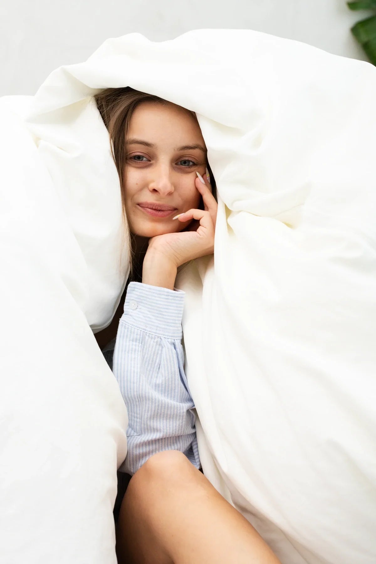 A woman resting under a white duvet pulled over her head.