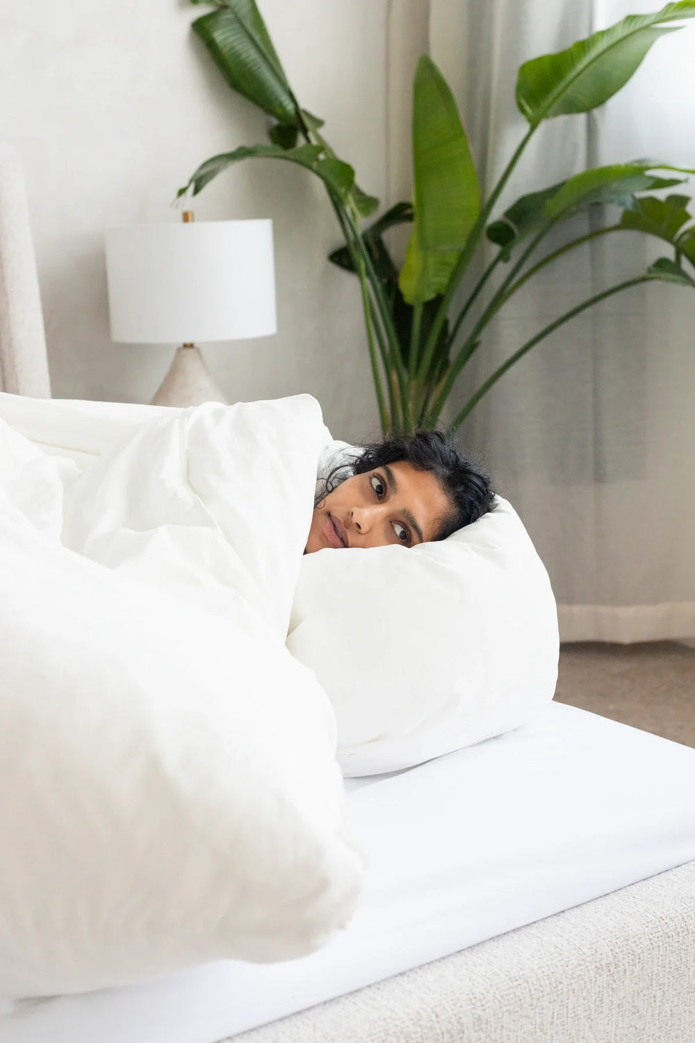 A woman lying on her side beneath a white duvet.