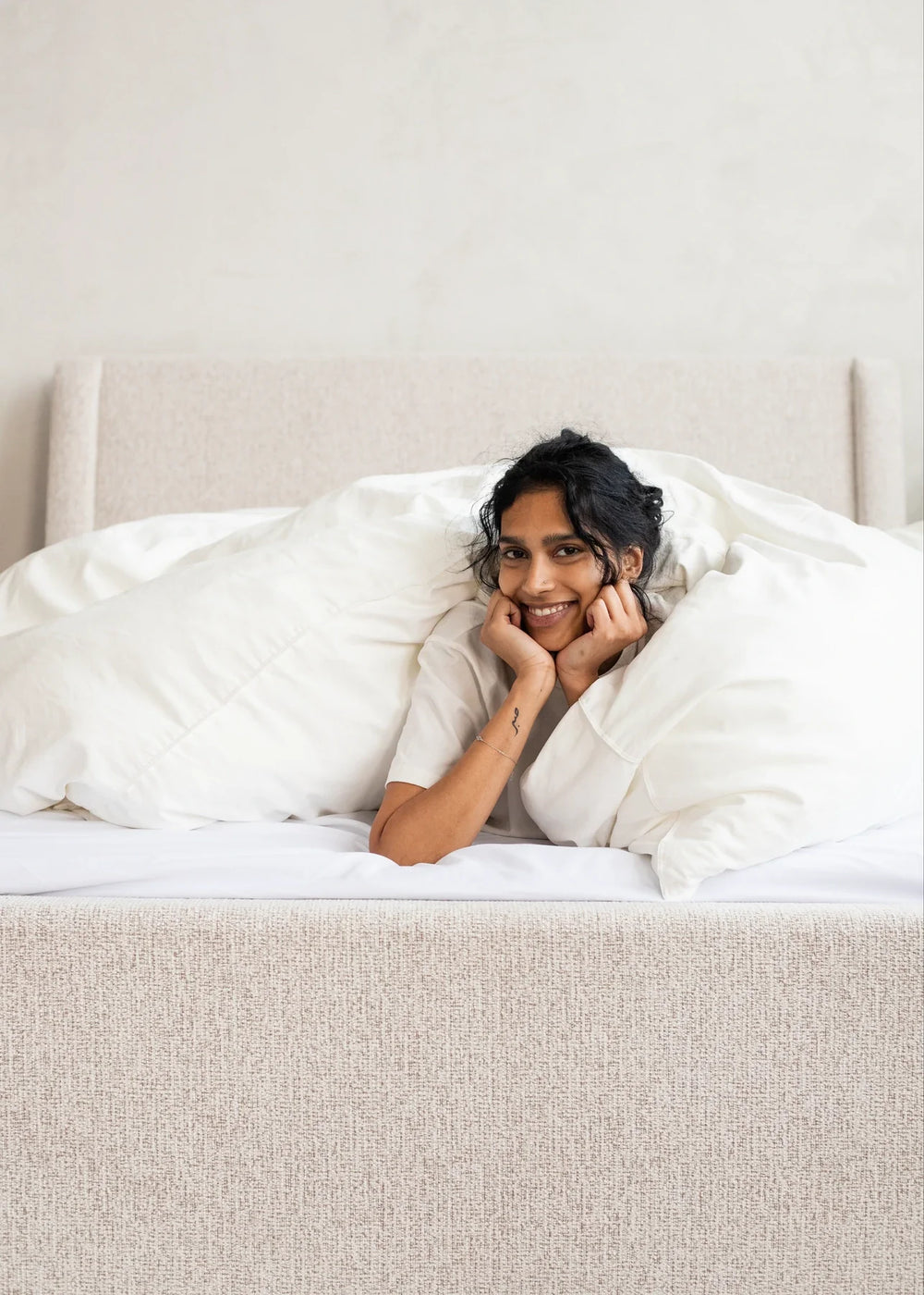 A woman resting her chin in her hands on a white duvet.
